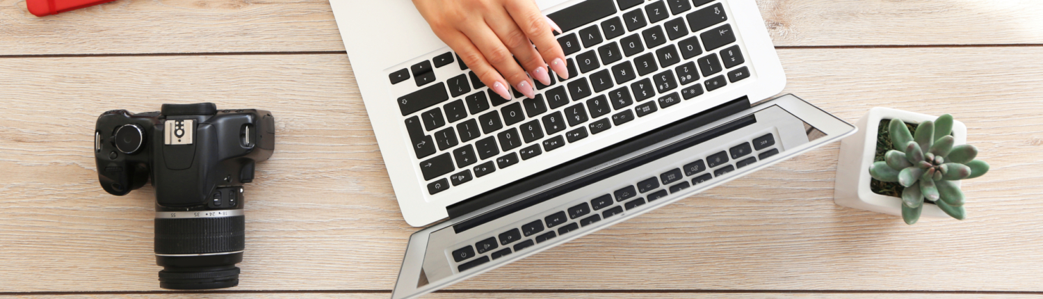 Eine Frau arbeitet am Laptop, neben ihr liegt eine Fotokamera, ein Wecker und ein Coffee To Go - Martina Wagner Immobilien