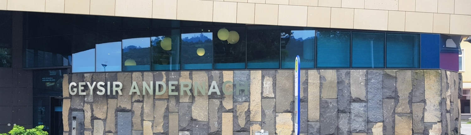 Blick auf das Geysirzentrum in Andernach mit einer Bank und dem Bushaltestellenschild und Mülleimer im Vordergrund - Martina Wagner Immobilien