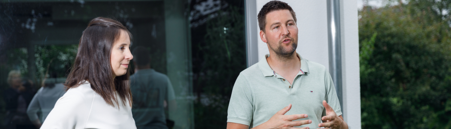 Beratungsgespräch Beratungsgespräch. Ein junges Paar steht im Garten vor einer modernen Hausfront und erklärt etwas - Martina Wagner Immobilien