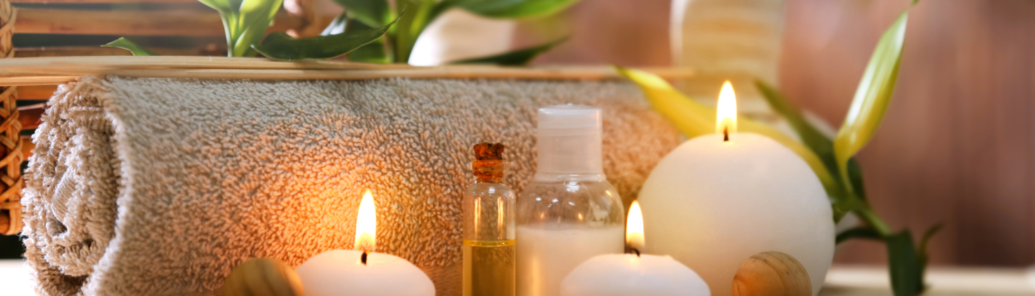 Kerzen und ein Duftöl vor einem Handtuch drapiert mit Pflanze und Bambus im Hintergrund - Martina Wagner Immobilien
