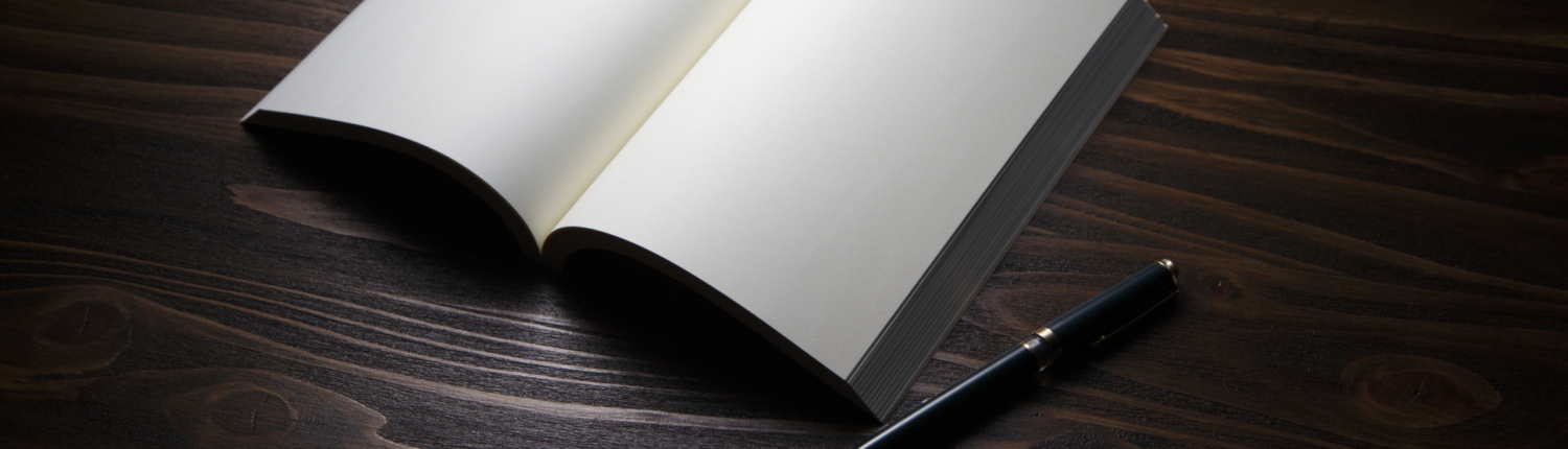Ein aufgeschlagenes reinweißes Notizbuch liegt auf einem dunklen Holztisch, daneben ein schwarzer Füller- Martina Wagner Immobilien