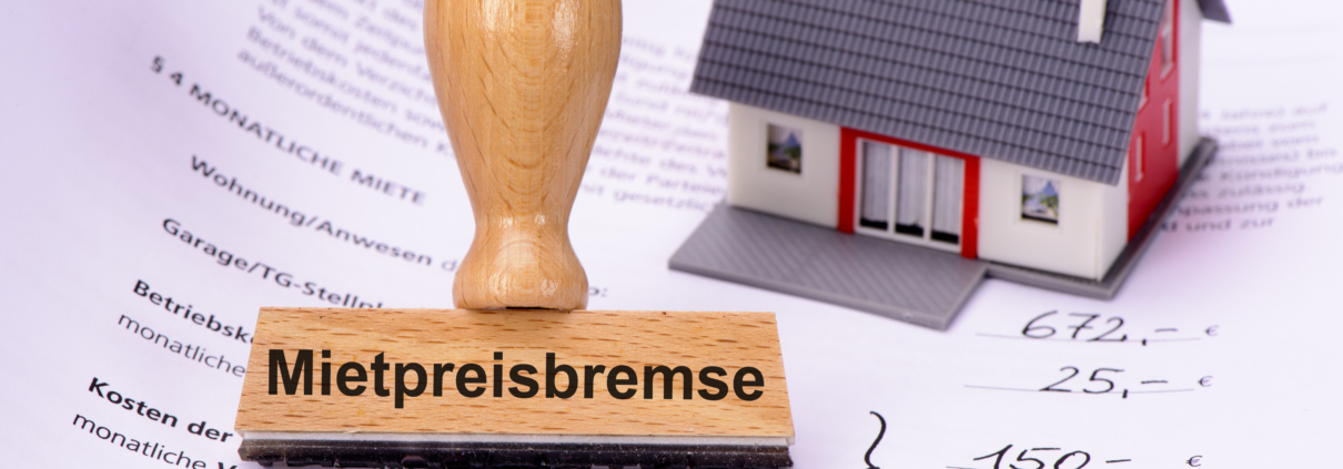 Mietpreisbremse steht auf einem Stempel, der auf einem Mietvertrag steht. Daneben befindet sich noch das Modell eines Hauses - Martina Wagner Immobilien