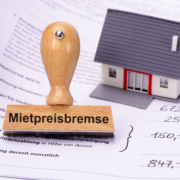 Mietpreisbremse steht auf einem Stempel, der auf einem Mietvertrag steht. Daneben befindet sich noch das Modell eines Hauses - Martina Wagner Immobilien