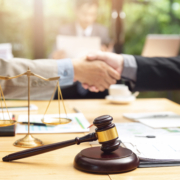 Ein Handschlag besiegelt einen Vertrag im Vordergrund sieht man eine Waage sowie einen Richterhammer und Dokumente - Martina Wagner Immobilien