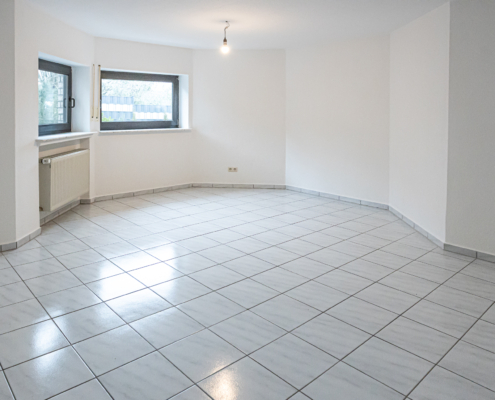 Wohnzimmer Souterrainwohnung mit weißen Fliesen, weißen Wänden, Blick auf einen Erker mit 2 Fenstern