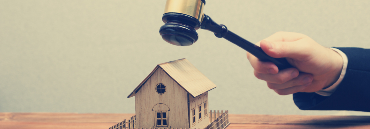 Richterhammer wird von einer männlichen Hand über das Modell eines Einfamilienhauses gehalten.