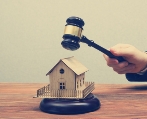 Richterhammer wird von einer männlichen Hand über das Modell eines Einfamilienhauses gehalten.