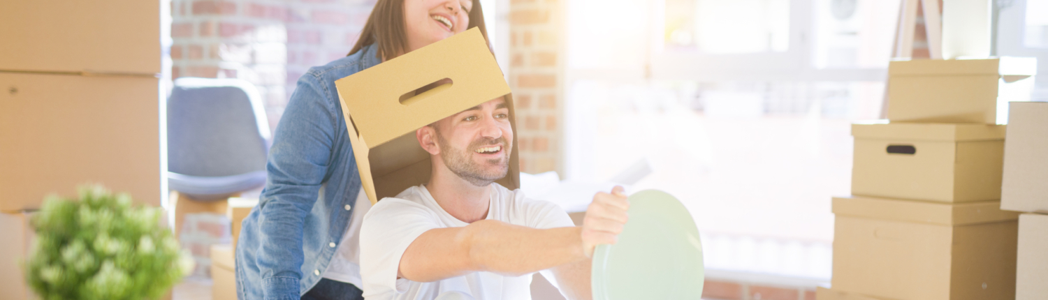 Funny and crazy couple having fun riding a cardboad box as a car, smiling happy and laughing at new home