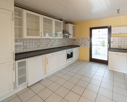 große helle Küche im Landhausstil mit Tür zum Wintergarten, hellen Fliesen und einer weißen Decke - Martina Wagner Immobilien