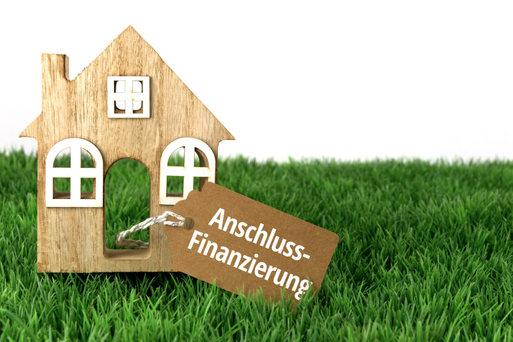 Ein Holzhaus (eindimensional) befindet sich auf einer Wiese, daran hängt ein Schild mit der Aufschrift Anschlussfinanzierung