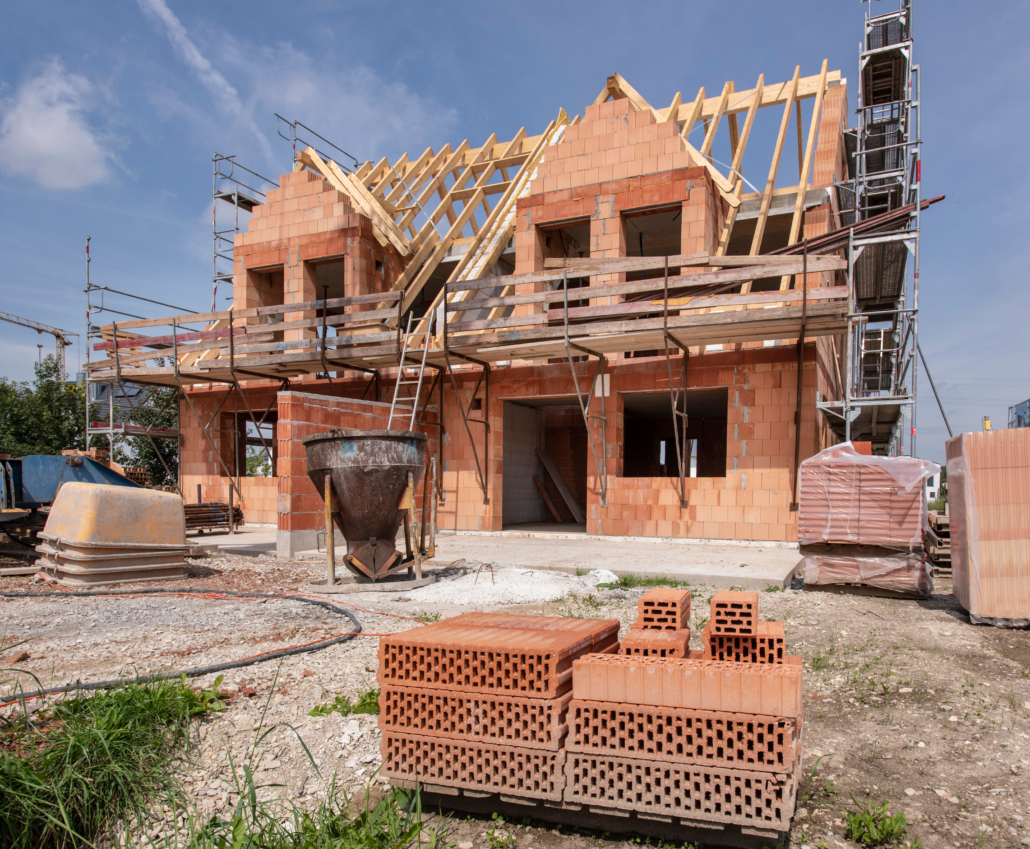 Das Bild zeigt einen Rohbau mit roten Ziegeln und einem Holzdachstuhl
