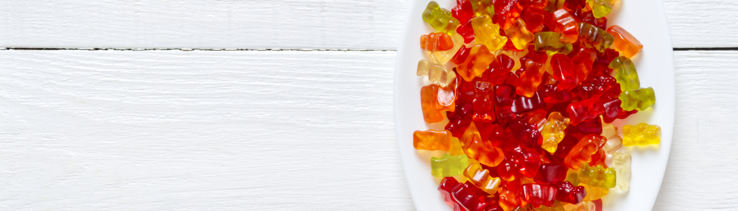 Gummy bears in a plate on a white wooden background. Bright jell