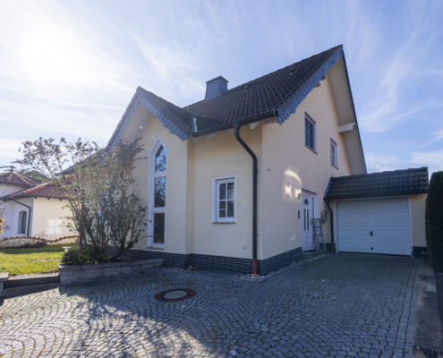 Seitliche Außenansicht der Immobilie in Oberlützingen. Gepflasterte Einfahrt, Garage und Vorgarten sind zu sehen