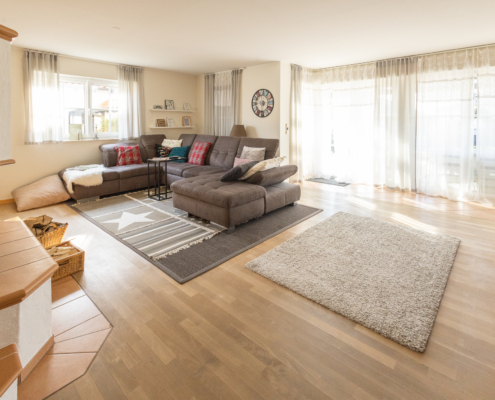 helles Wohnzimmer mit Parkettfußboden, vielen Fenstern und einem zentralen Sofa