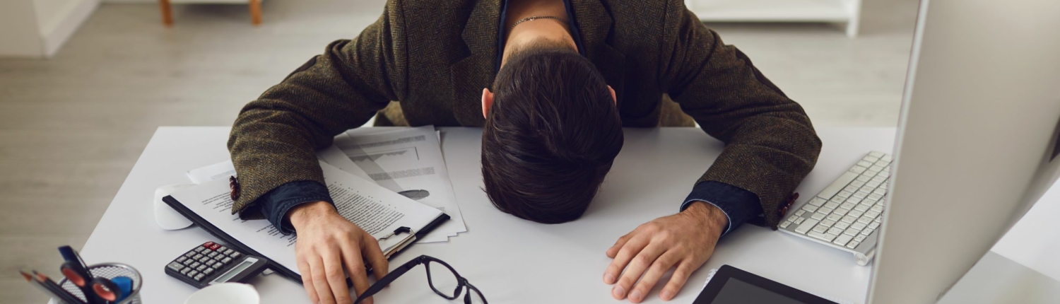 stress Man sieht einen Mann mit Kopf auf dem Schreibtisch und verschieden Arbeitsutensilien