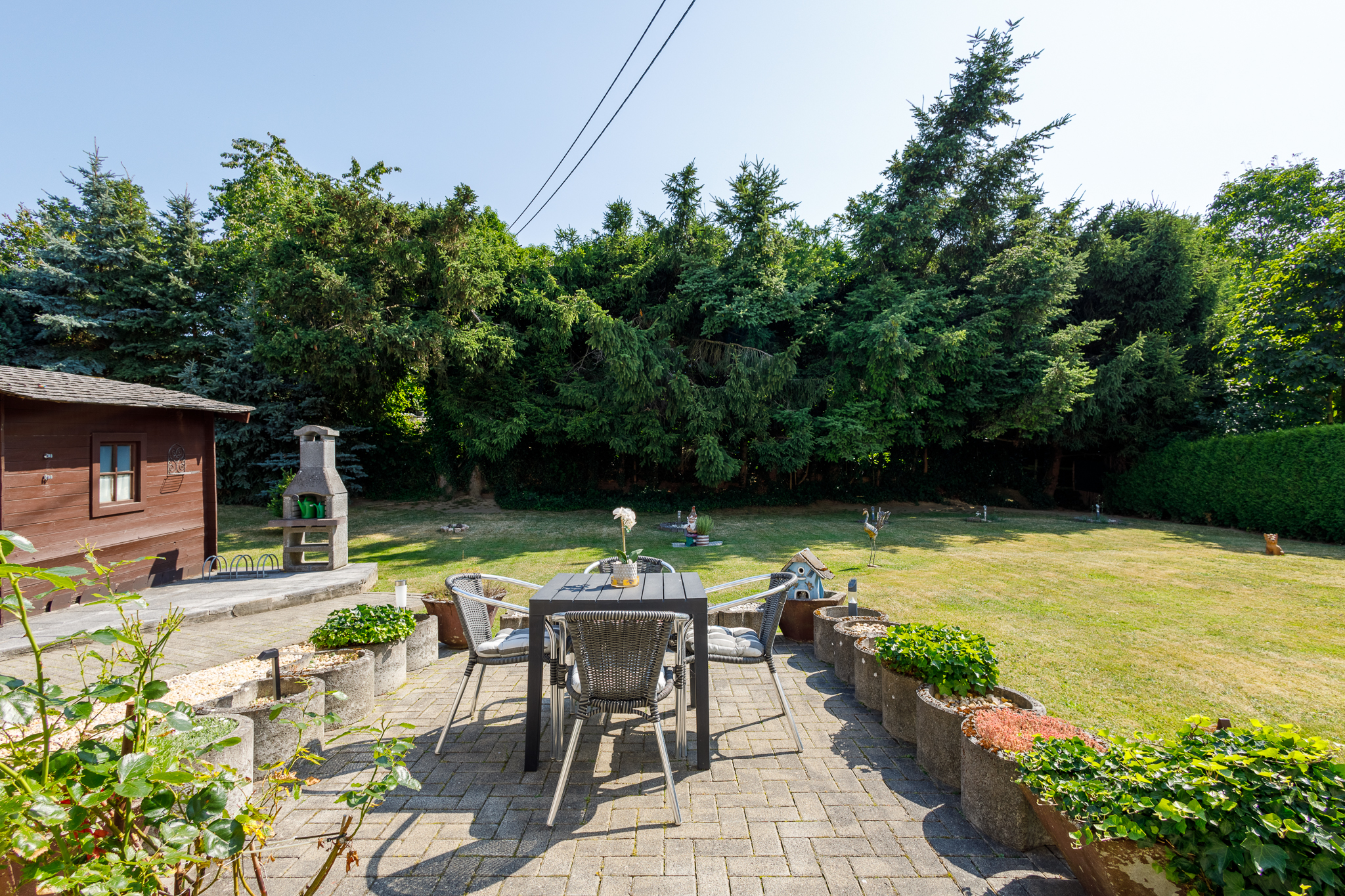 sonnige Terrasse mit Blick ins Grüne man sieht einen gepflasterten Terrassenbereich mit Blick in den Garten und Gartenhaus auf der linken Seite.
