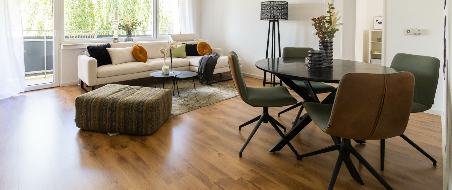 heller Wohnbereich mit modernem Laminatboden, im Hintergrund Fensterfront zum Balkon, modern Möbliert, rechts Zugang zu weiteren Zimmern