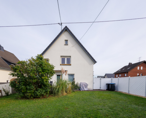 Blick aus dem Garten auf das Einfamilienhaus Blick aus dem Garten auf das Einfamilienhaus, viel Rasen im Vordergrund, Strauch rechts, weißer Zaun links, dahinter sieht man Klinkerhaus.