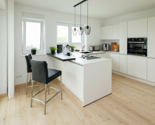 weiße moderne Küchenzeile, mit Theke davor 2 schwarze Hochstühle