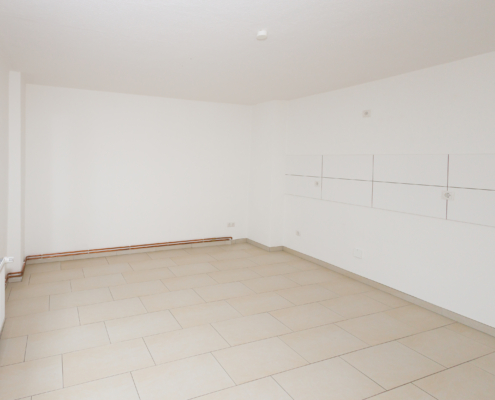 helle Wohnküche mit viel Raum Man sieht einen Raum mit hellen Fliesen und einem weißen Fliesenspiegel an der Wand, links ist ein Fenster.