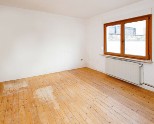 Zimmer mit Echtholzdielenboden, Wände und Decke sind weiß, rechts befindet sich ein großes Holzfenster, darunter ein Heizkörper.