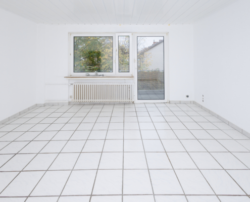 Blick aus dem Wohnzimmer in Richtung Balkon Wohnzimmer mit weißen Fliesen, Wänden und Decke, zentral ein Fenster mit Balkontür darunter ein Heizkörper