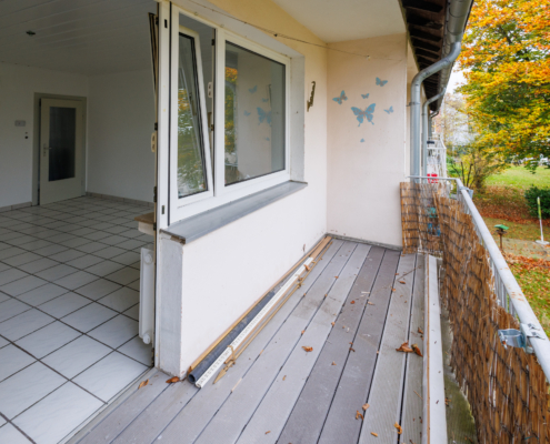 Blick vom schönen Balkon ins Wohnzimmer Balkon mit Blick ins herbstliche Grün rechts, links steht die Balkontür zum Wohnzimmer offen, man sieht es ist weiß gefliest.