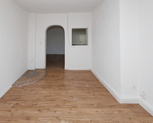 Raum mit weißen Decken und Wänden, Boden Holz, zentral Torbogen als Durchgang und Durchreiche rechts,